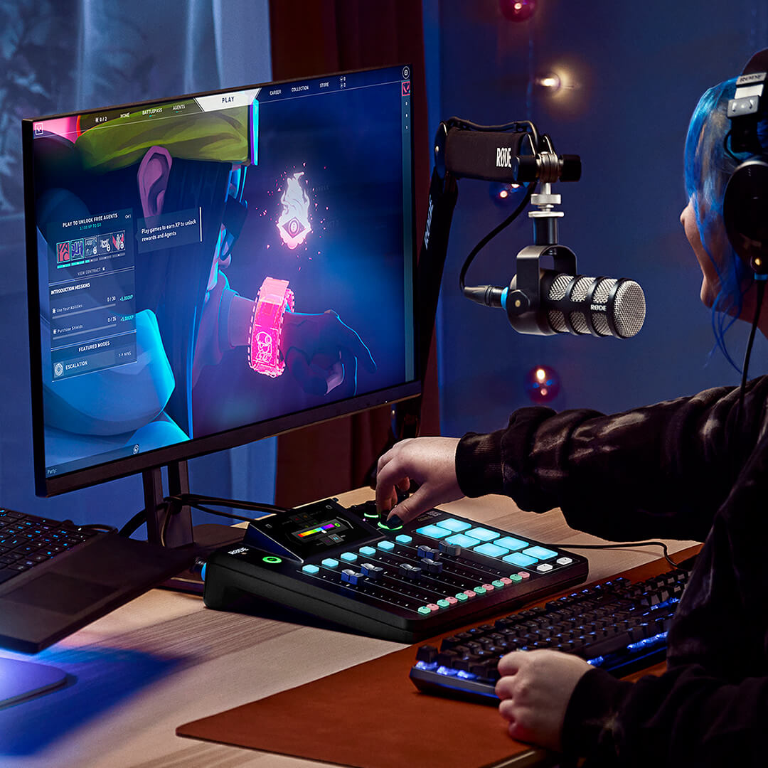 Gamer streaming at a desk with a RØDECaster Pro II, its SMART pads lit, next to a keyboard and monitor.